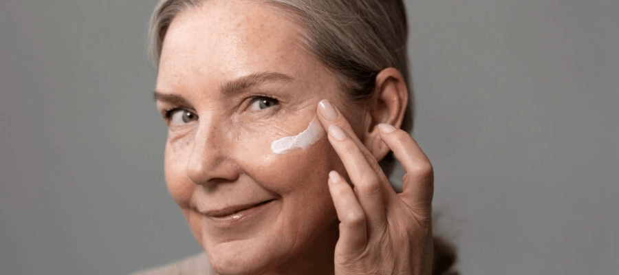 mulher sorridente com pele madura passando protetor solar para cuidar do seu rosto