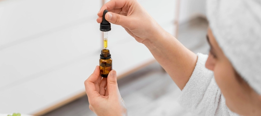 Mulher no banheiro com uma toalha enrolada na cabeça abrindo um frasco de óleo essencial.