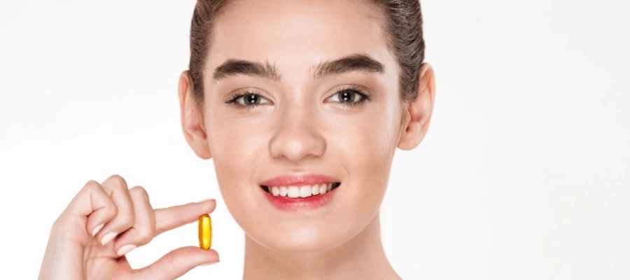 Mulher sorri e segura cápsula amarela de suplemento com fundo branco