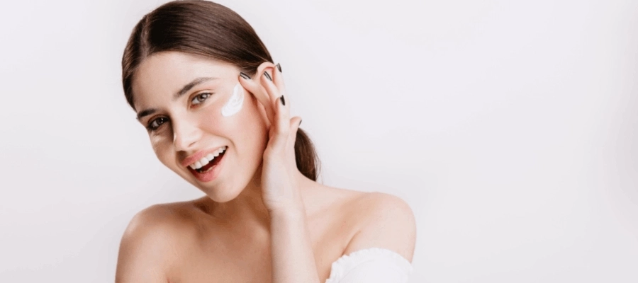 Mulher de cabelo castanho sorri e aplica protetor solar no seu rosto