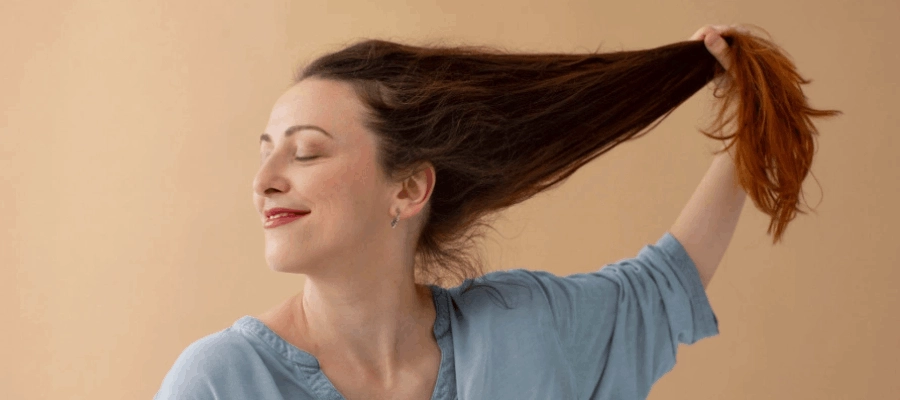 Mulher sorridente e vestindo uma blusa azul segura o seu cabelo longo e de coloração castanho.